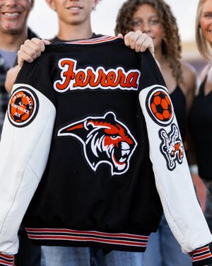 Black and white varsity letterman jacket with Ferrera name, tiger mascot patch, and soccer ball emblem.