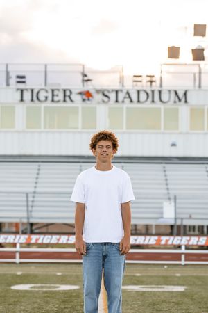 Young man in white t-shirt and jeans standing at Erie Tigers Stadium football field.