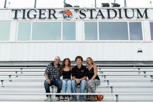Family of four smiling together in the bleachers at Tiger Stadium on a sunny day.