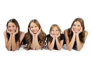 Four smiling girls with brown hair lying down together posing for a portrait on white background.