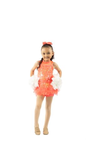Young girl in coral sequin dance costume with white pom-poms and matching bow, posing in dance recital outfit.
