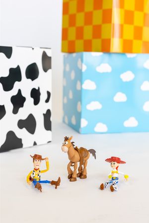 Small Toy Story figurines arranged in a playful scene with checkered pattern and cloud backgrounds.