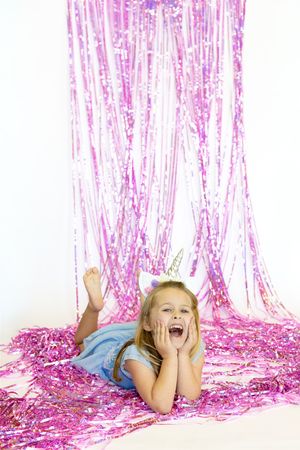 Child lying on floor surrounded by sparkly pink tinsel and streamers in festive party setting.