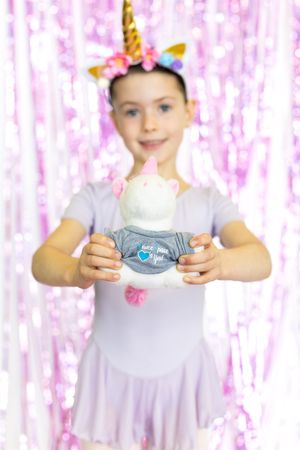Children in pastel dresses against sparkly pink backdrop holding party favors.