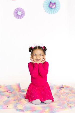 Child in bright red dress sitting on colorful floor with decorative paper fans on wall.