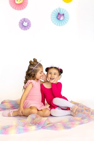 Two children in pink and red dresses sitting together on sparkly backdrop with paper decorations.