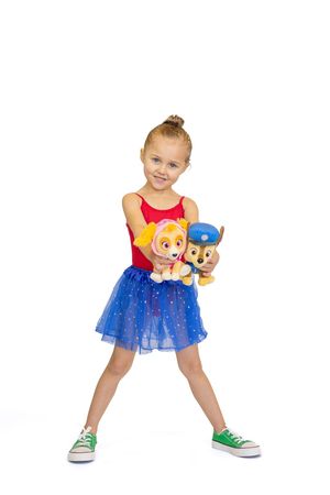 A young dancer in a red and blue tutu dress poses with Paw Patrol plush toys against a white background.