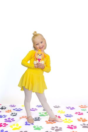 Young dancer in yellow leotard and tutu poses on floor with colorful paw print decorations.