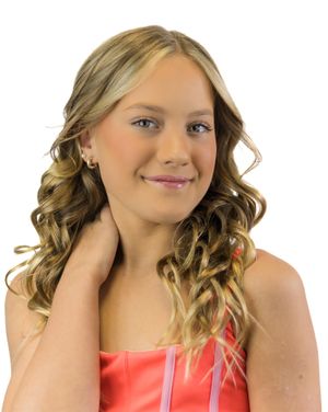 Person with wavy blonde hair and coral top poses cheerfully against white backdrop.