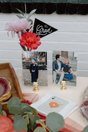 Graduation party table display with photos, floral arrangement, and a black pennant flag reading Grad.