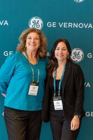 Two women smiling together at a GE Vernova corporate event in front of a branded teal backdrop.