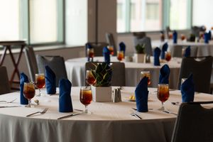 Elegant banquet tables set with blue napkins, red cocktails, and white tablecloths in a bright event venue.