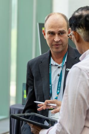 Professional man in suit with lanyard engaged in conversation at business conference event.