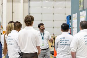 Team members in white uniforms listening to a presenter during a workplace training session in an industrial facility.