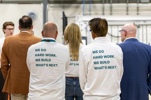 Group of people wearing white shirts with 'We Do Hard Work. We Build What's Next.' printed on the back.