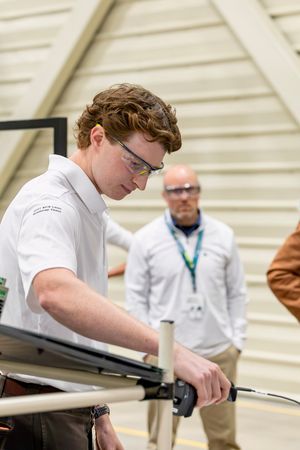 Young man in safety glasses working on technical equipment at an indoor engineering competition.