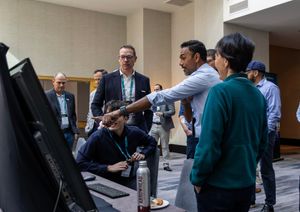 Professionals networking at a conference, with attendees discussing near monitor displays in a modern convention center.