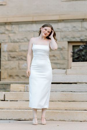 Young woman in elegant white midi slip dress posing on stone steps outside a historic building.