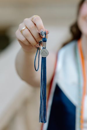 Close-up of hand holding a navy blue graduation tassel with decorative medallion and rings visible.