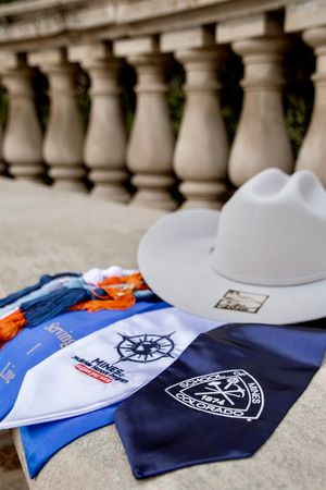 Colorado School of Mines graduation items including a white cowboy hat, blue sashes, and navy bandana on stone steps.