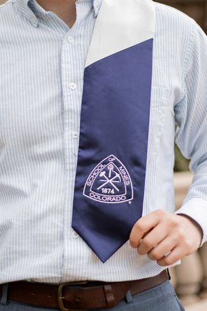 Navy blue Colorado School of Mines graduation stole with embroidered crest worn over a light blue button-down shirt.