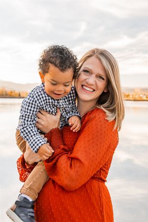 A bright orange sweater adds warmth to this intimate family photoshoot by a lake at sunset.