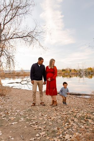 Family enjoying a fall day by the lake with fallen leaves scattered on the ground.