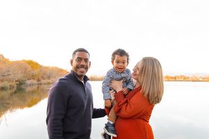 A family enjoys a playful autumn photoshoot together outdoors near a lake at sunset.