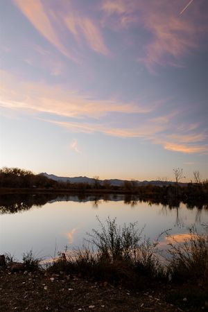 Tranquil lake landscape at sunset with mountains in the background and pink clouds reflecting on water.