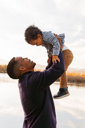 Playful moment between parent and child against a serene lakeside backdrop.