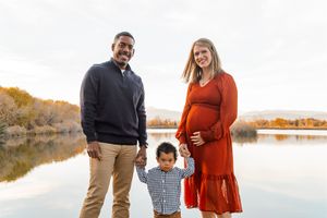 Family enjoying a fall photoshoot by a lake with autumn trees and rocks in the background.