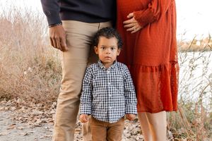 Casual outdoor family photos captured on a rocky beach with fall foliage in the background.