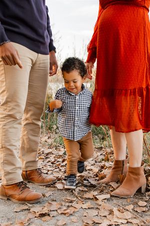 Family members in khaki pants and boots stand together on fallen autumn leaves with a small child in a checkered shirt.