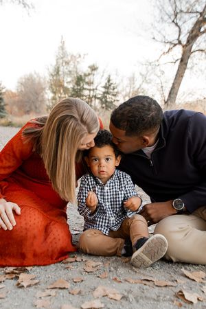 Candid moments captured on the ground during a fall family photoshoot with autumn leaves scattered around.