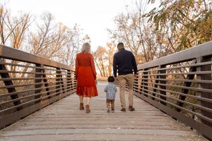 A family walks together on a wooden bridge during a sunset photoshoot.