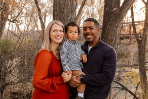 A family in coordinating red and navy outfits poses together outdoors during autumn among bare trees.