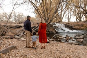 A couple and their dog walk along a rocky creek bed in an autumn forest landscape.