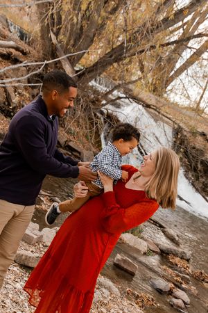 A family embraces and laughs together under autumn trees with fallen leaves.