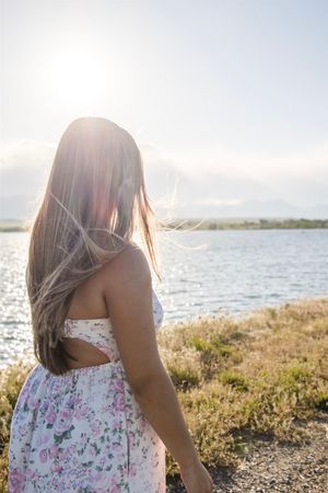 Side view of woman in floral dress standing by waterfront during golden hour.