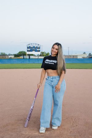 A casual pose on a softball field with a bat while wearing jeans and a crop top.