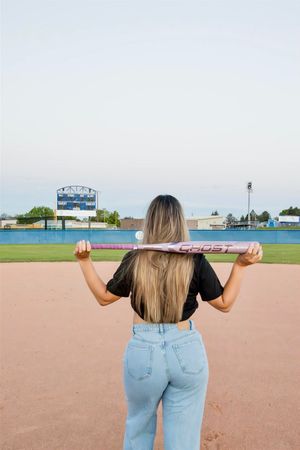 Back view of someone holding a softball bat on a field with stadium letters visible.