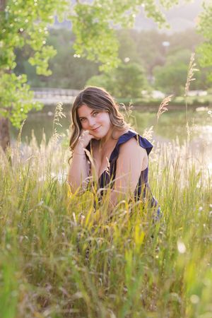 A person in a navy blue dress sits peacefully among tall grass and wildflowers in golden sunlight.