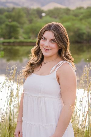 Portrait taken near a lake with tall grasses as a person in a white summer dress smiles at the camera.