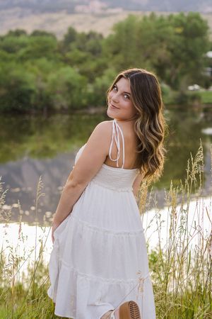 A white flowy sundress blows in the breeze near a lakeside meadow with tall grass and natural scenery.