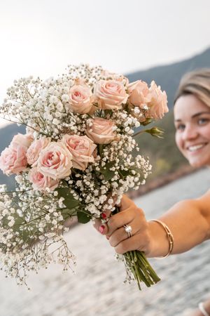 Smiling bride holds a bouquet of pink roses and baby's breath, wearing an engagement ring and gold bracelet.