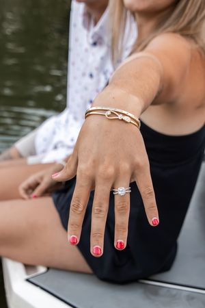 Close-up of woman's hand displaying diamond engagement ring with red nails and gold bracelets on a boat.