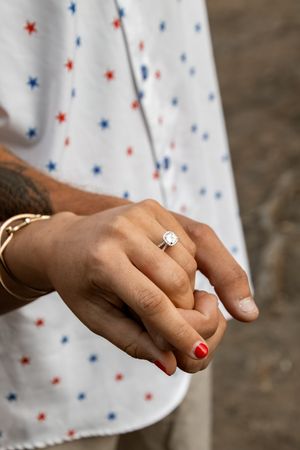 Close-up of a woman's hand wearing a diamond engagement ring with red nails and a gold bracelet.