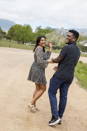 A couple dances playfully on a dirt path with mountains and spring trees in the background.