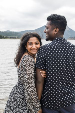 A couple poses romantically by a mountain lake, wearing coordinated black and white patterns.