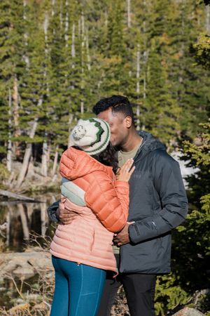 A couple shares a tender moment among rocks overlooking a mountain lake.